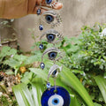 Linked silver tone eye motifs with dangling blue beads and a round blue pendant held in front of greenery