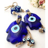 Angled close-up of two blue Hamsa evil eye pendants with eye beads and tan cords