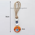 Orange evil eye hanging with a blue cube bead and knotted tan loop, with 18 cm and 4 cm annotations