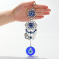Round evil eye wall hanging held in a hand, with silver tone scrollwork medallions, blue eye beads and coin-shaped charms.