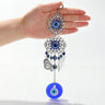 Round evil eye wall hanging held in a hand, with silver tone scrollwork medallions, blue eye beads and coin-shaped charms.