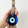 Hand holding the blue lower eye pendant and tan cord-wrapped center of the tassel hanging