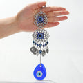 Teardrop evil eye wall hanging held in a hand, with silver tone scrollwork medallions, blue eye beads and coin-shaped charms.