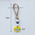 Yellow evil eye hanging with a tan cord loop and blue cube bead, with 18 cm and 4 cm annotations