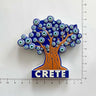 Tree-shaped magnet with an orange trunk, blue eye-pattern canopy and CRETE base beside ruler markings.
