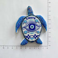 Blue and white turtle-shaped magnet with an eye on its shell and CRETE lettering beside ruler markings.