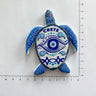 Blue and white turtle-shaped magnet with an eye on its shell and CRETE lettering beside ruler markings.