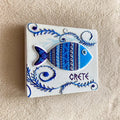 White rectangular magnet with a raised blue and turquoise patterned fish, curling foliage and CRETE lettering, shown at an angle.