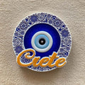 Round blue eye magnet with a blue and white floral border and orange Crete script across the bottom.
