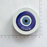 Round blue and white eye magnet with Greece lettering and a subtle wavy border beside ruler markings.