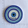 Round blue and white eye magnet with concentric wave and dot borders and CRETE lettering beside ruler markings.