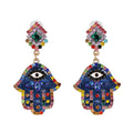 Blue Hamsa earrings with black-and-white eyes, multicolored accents and green centers in diamond-shaped tops.