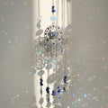 Silver tone Hamsa suncatcher with a blue central eye, clear faceted discs, dark blue beads and small hand charms.