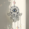 Close view of a silver tone Hamsa hand with curling open scrollwork, small blue accents and a blue evil eye in the palm.