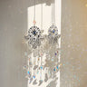 Star-drop and crescent-moon Hamsa suncatchers hanging side by side against a sunlit wall.