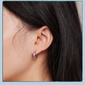 Side view of a blue evil eye hoop earring with alternating clear hearts worn on an ear