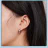 Side view of a blue evil eye hoop earring with alternating clear hearts worn on an ear