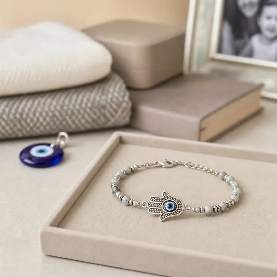 A sharply focused Hamsa bracelet on a tray with a blurred evil eye charm, textile, keepsake box, and book-like surface in the