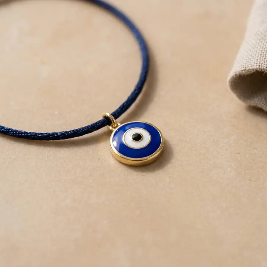 A macro view of a single evil eye charm with sharp blue enamel detail on a beige surface and a soft fabric edge nearby.