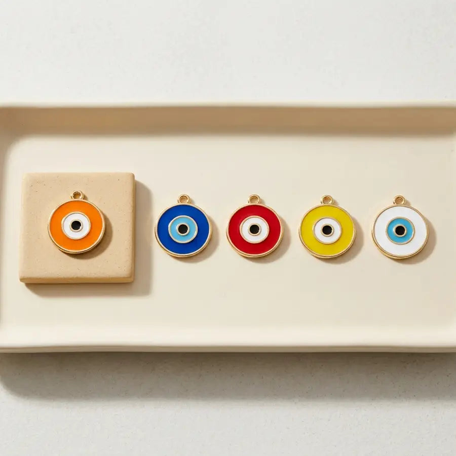 Five round evil eye charms in orange, blue, red, yellow, and white arranged in a row on a pale tray.