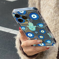Hand holding a phone in a clear case decorated with blue eyes, turquoise Hamsa hands and small outlined hearts.