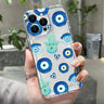 Clear phone case with blue eye circles, turquoise Hamsa hands and small hearts, shown on a light-colored phone.