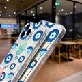 Two phones in clear cases with blue eye and turquoise Hamsa patterns, angled to show the side buttons and edges.