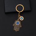 Black scroll Hamsa keychain with gold tone outlines, a blue palm eye and a separate round eye charm on a black background.