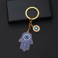 Blue scroll Hamsa keychain with gold tone outlines, a blue palm eye and a separate round eye charm on a black background.