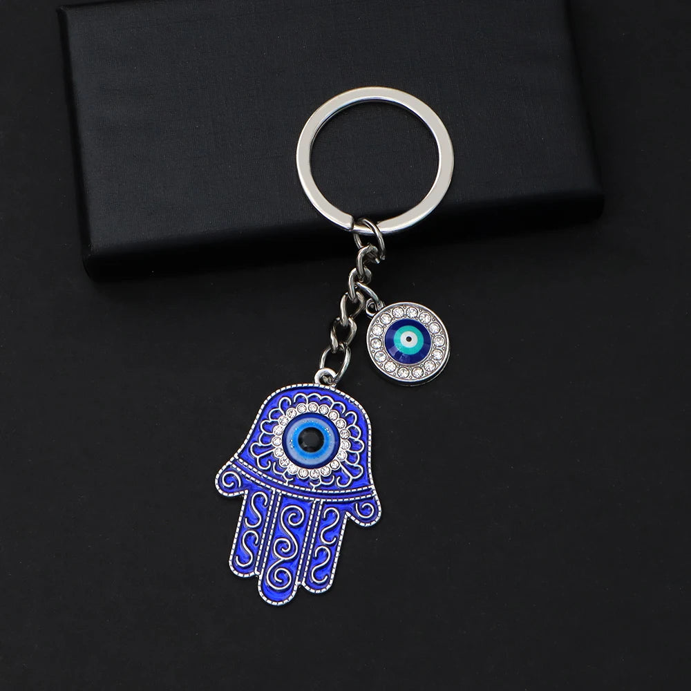 Blue scroll Hamsa keychain with silver tone outlines, a blue palm eye and a separate round eye charm on a black background.