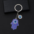 Blue scroll Hamsa keychain with silver tone outlines, a blue palm eye and a separate round eye charm on a black background.