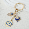Gold tone elephant cluster keychain with blue elephant, hamsa hand and round eye pendant, arranged diagonally with the ring at the upper right.
