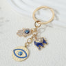 Gold tone elephant cluster keychain with blue elephant, hamsa hand and round eye pendant, arranged diagonally with the ring at the upper right.