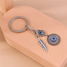 Hamsa medallion keychain laid diagonally on a peach block, showing a feather and two blue eye motifs.