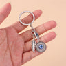 Hamsa medallion keychain held across an open hand, with a silver tone feather and round blue eye pendant.