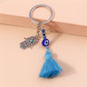 Blue Hamsa tassel keychain resting against a peach block, with the hand charm angled beside the eye beads.