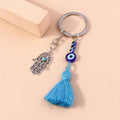 Hamsa keychain with blue eye beads and a fanned blue tassel, arranged beside a small peach block.