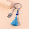 Hamsa keychain with blue eye beads and a fanned blue tassel, arranged beside a small peach block.