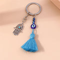 Blue tassel and eye bead strand hanging beside an open Hamsa charm, with the key ring above on a peach surface.