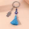 Blue tassel and eye bead strand hanging beside an open Hamsa charm, with the key ring above on a peach surface.