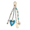 Keychain with a large blue heart-shaped eye pendant, small hamsa charm, decorated heart charm and cream tassel