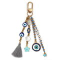 Keychain with HELLO letter beads, blue eye motifs, hamsa, flower and butterfly charms, and a grey tassel