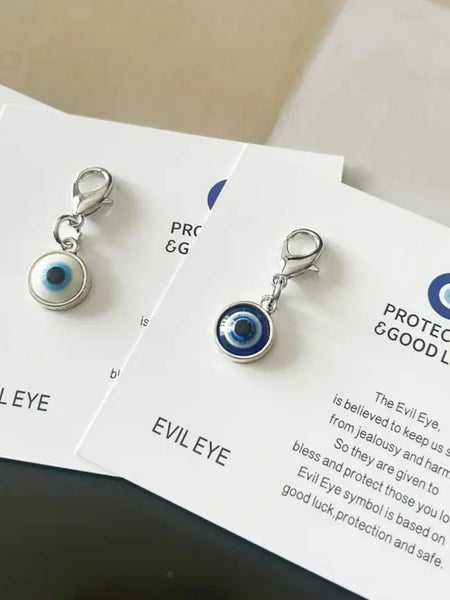 Blue and white round evil eye keychain charms with silver tone lobster clasps lying on overlapping printed cards.