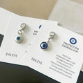 Blue and white round evil eye keychain charms with silver tone lobster clasps lying on overlapping printed cards.