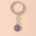 Round blue eye medallion with a raised dot border, suspended from a short silver tone chain and circular key ring.