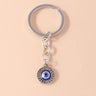 Round blue eye medallion with a raised dot border, suspended from a short silver tone chain and circular key ring.