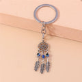 Silver tone flower-circle keychain resting against a peach block, with three blue beads above three feather charms.