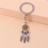 Silver tone flower-circle keychain resting against a peach block, with three blue beads above three feather charms.