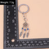 Three bead feather keychain beside an L-shaped ruler, with a weight label in the upper left corner.