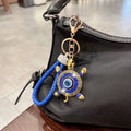 Blue turtle evil eye keychain clipped to a black handbag, with a blue braided loop and blue shell accents.